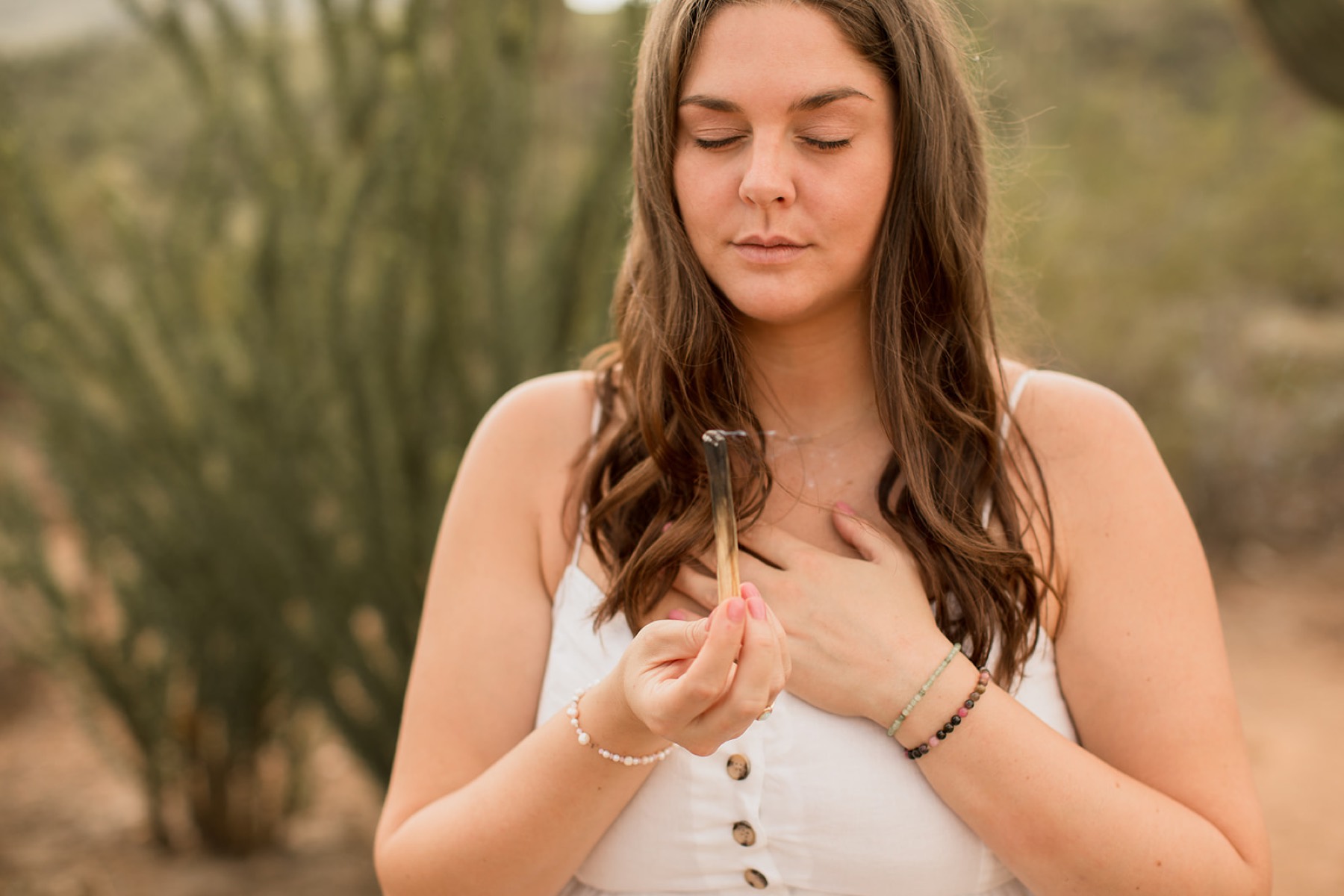 Heather Flynn holding palo santo at her heart, hand on her chest, in the sunlit desert